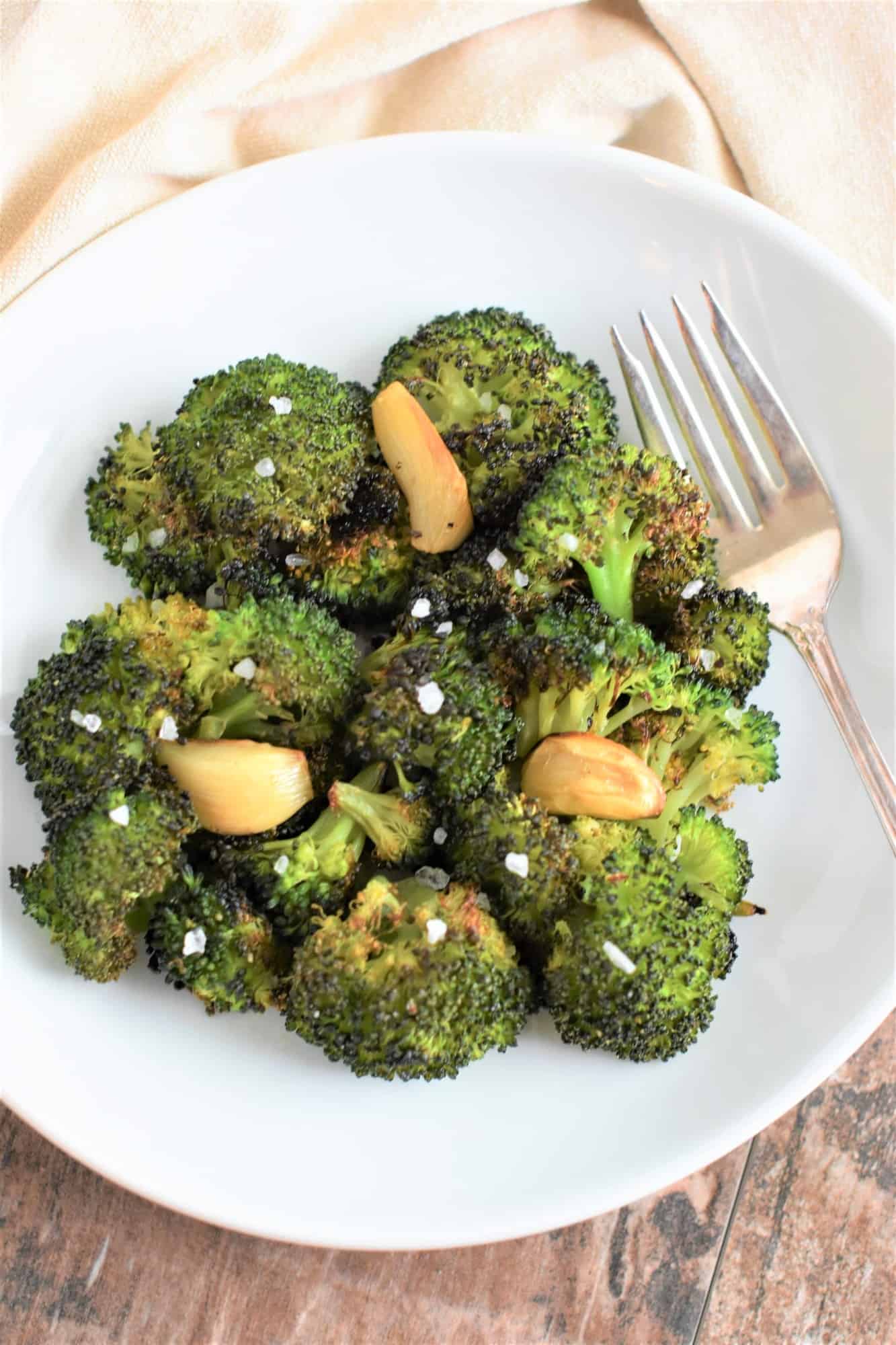 overhead of roasted broccoli with garlic garnished with salt on white plate