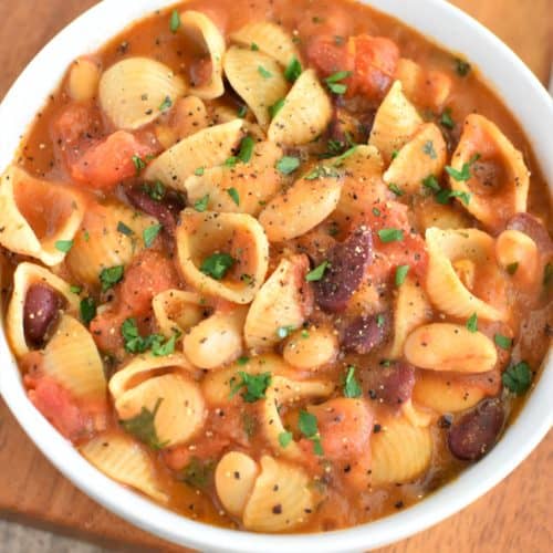 close-up overhead of pasta fagioli in white bowl garnished with pepper and parsley