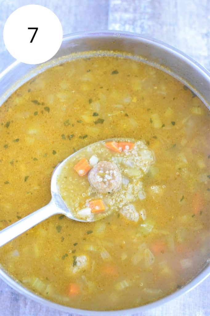 meatball and quinoa being held up on a spoon over the soup after being cooked