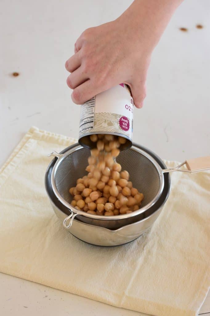 pouring a can of chickpeas into a mesh strainer over a mixing bowl to drain the liquid