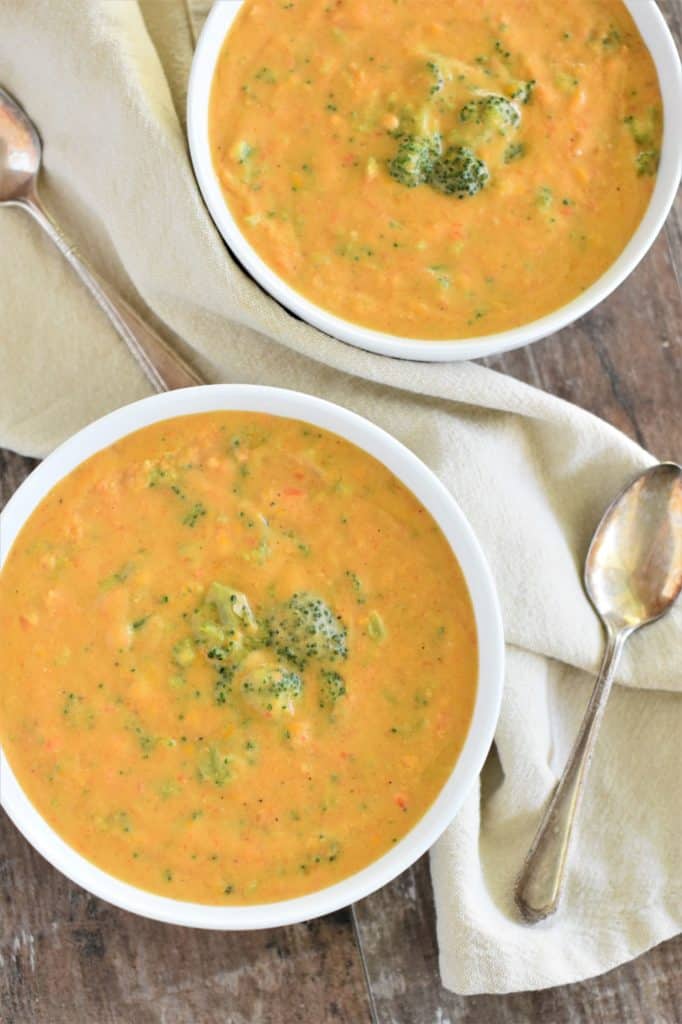 overhead of two bowls of vegan broccoli cheese soup with spoons next to them on kitchen napkin