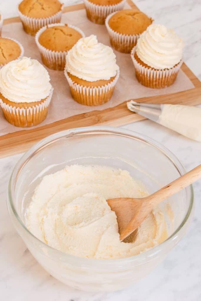 frosting in mixing bowl with some frosted cupcakes behind it and some without frosting