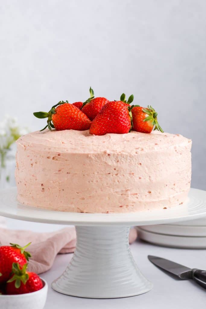 front view of cake on a white cake stand topped with fresh strawberries