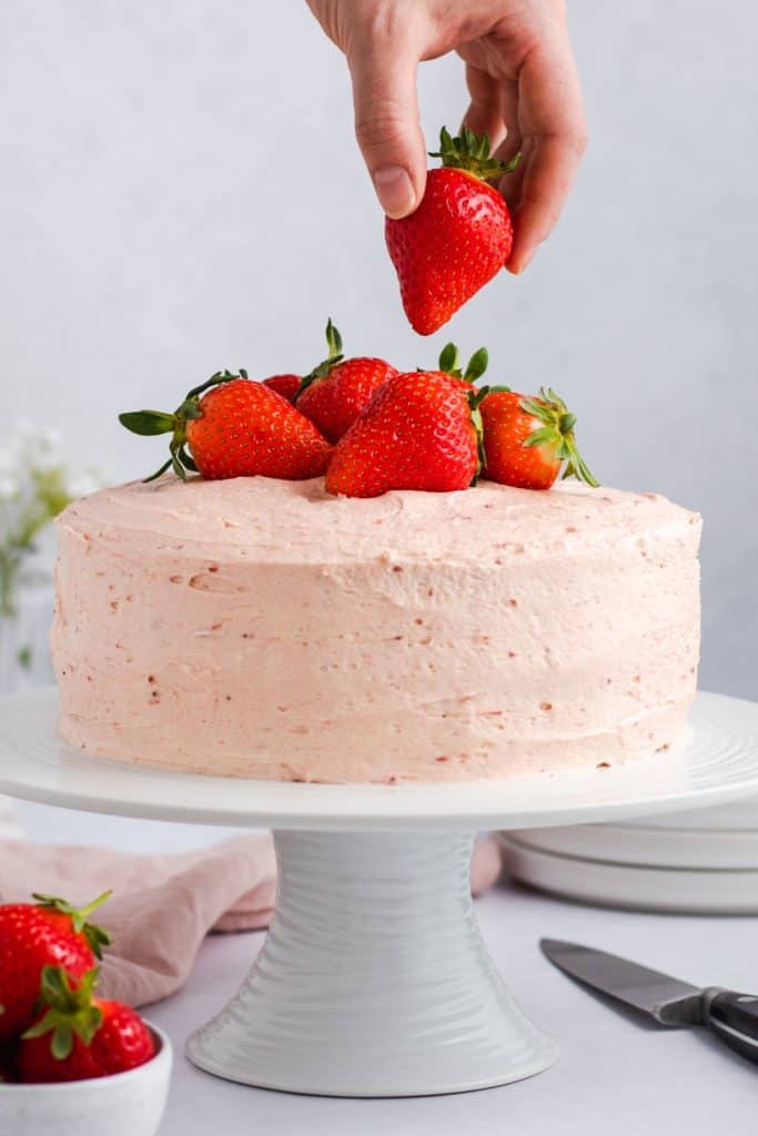 hand placing a strawberry on top of the cake