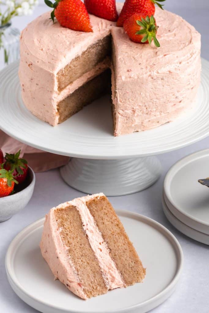 slice of cake on a white plate with the rest of the cake on the cake stand behind it