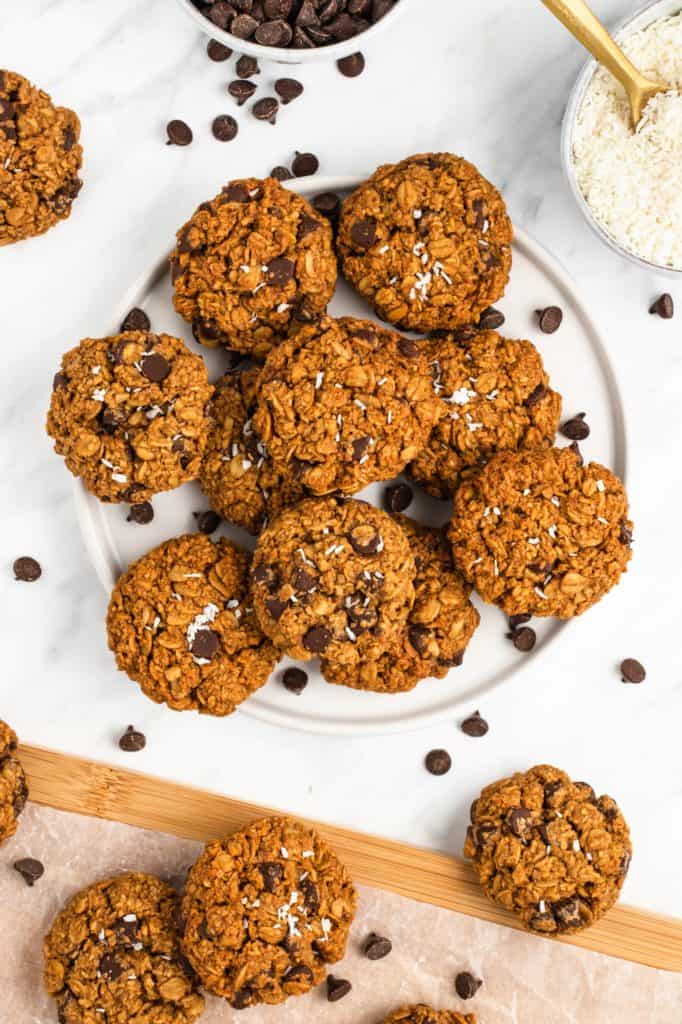 some cookies in a pile on a white plate with others on wooden board