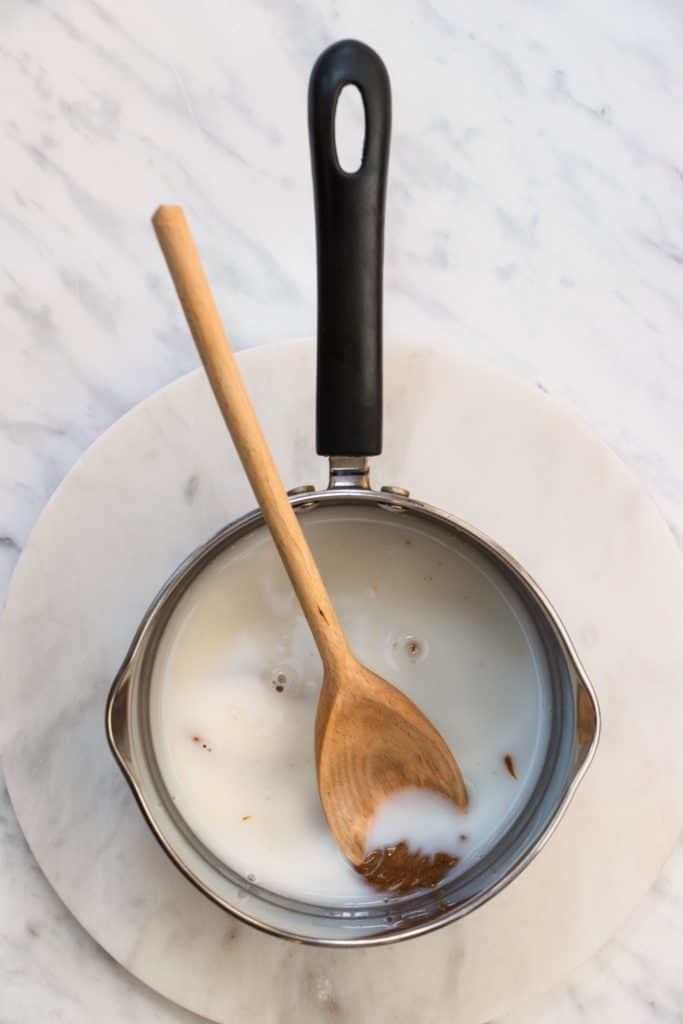 almond milk, almond butter and maple syrup in a saucepan with a wooden spoon in it