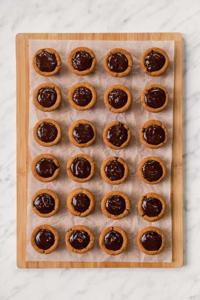 cookie cups on wooden board with parchment after being filled with the chocolate mixture