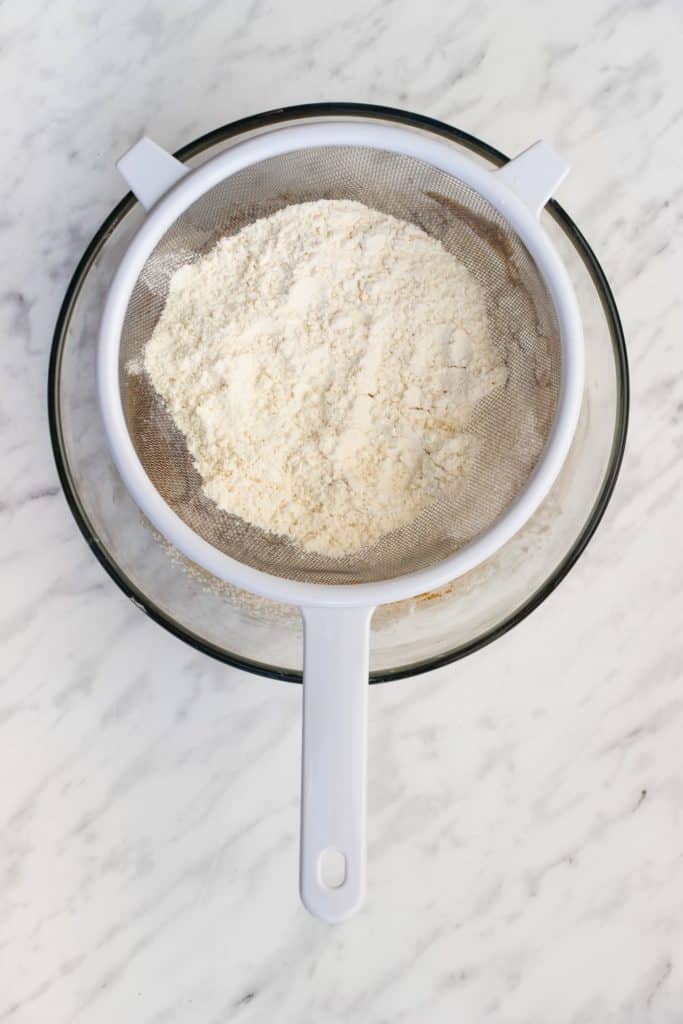 sifting dry ingredients into wet ingredients in mixing bowl