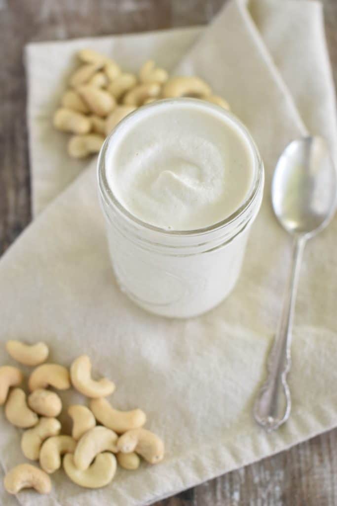 slightly overhead front view of mayo in a mason jar on kitchen towel with some cashews around and a spoon next to it