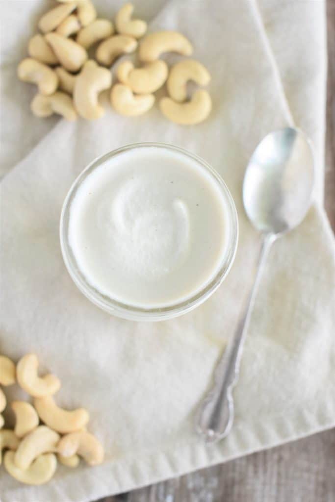 overhead view of mayo in a mason jar on kitchen towel with some cashews around and a spoon next to it