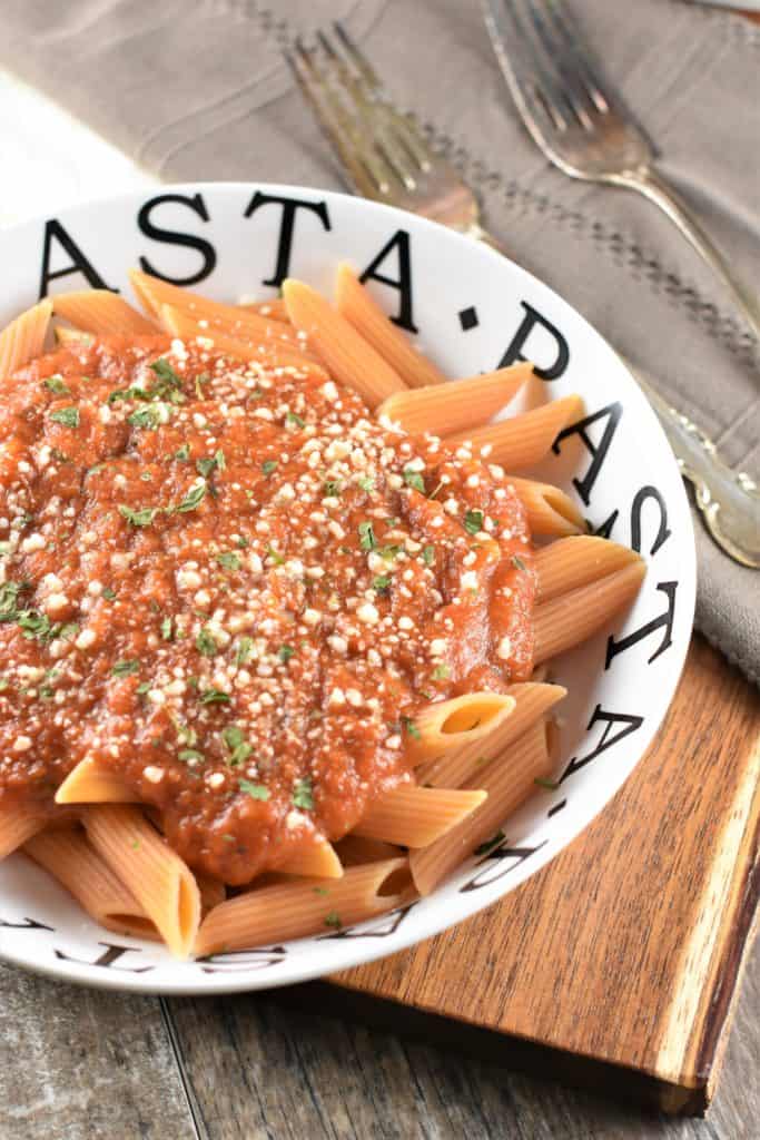 red lentil penne pasta in pasta bowl with pumpkin tomato sauce garnished with grated cheese and parsley