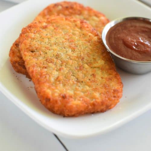 two hash brown patties on white plate garnished with salt and pepper and a side of ketchup