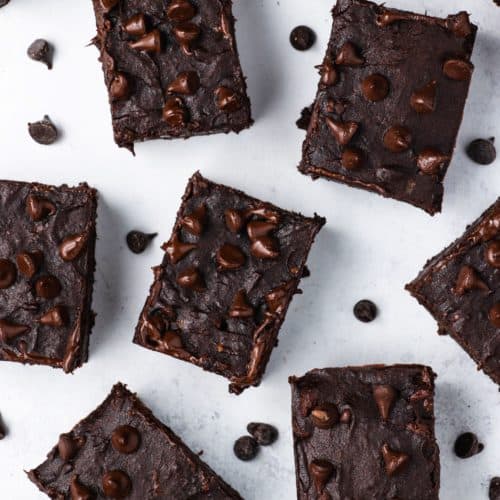 overhead of sliced brownies on white surface with chocolate chips scattered around