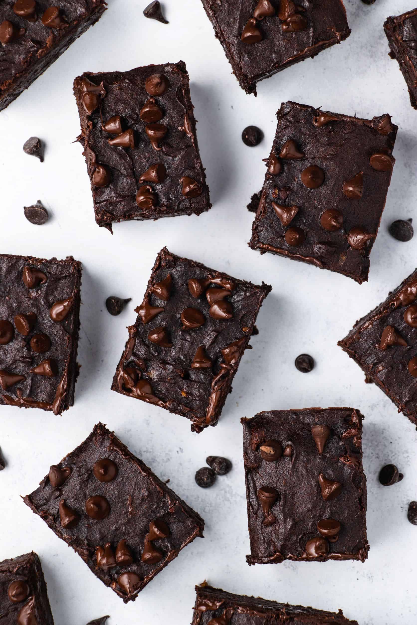 overhead of cut brownies on a white surface with chocolate chips around