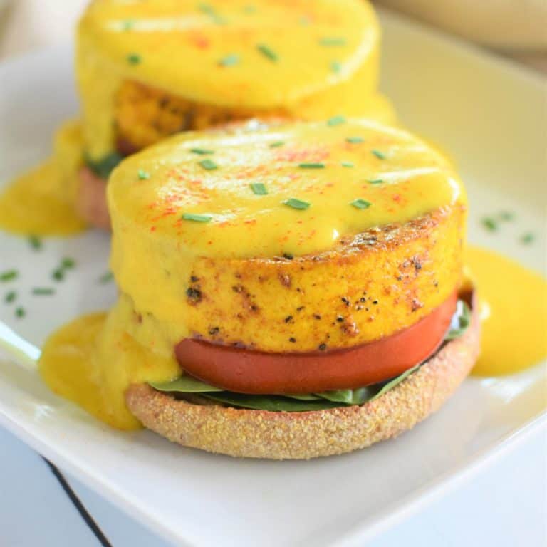 close-up of serving of vegan eggs Benedict on a white plate with another behind it partially cut off