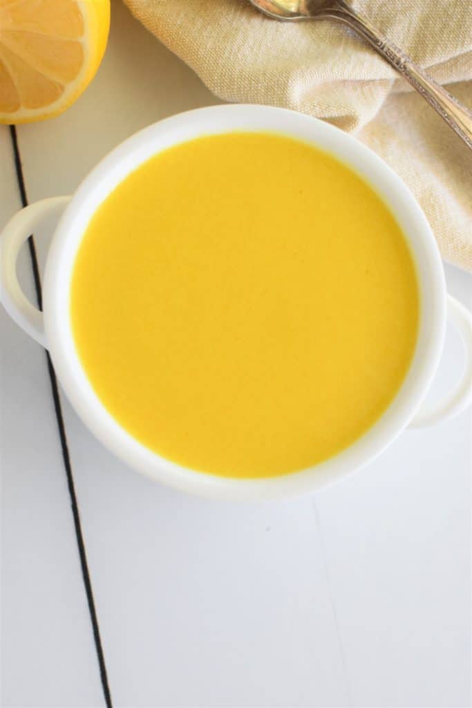 overhead of vegan hollandaise in a small white serving bowl with part of a lemon and part of a spoon in view behind it