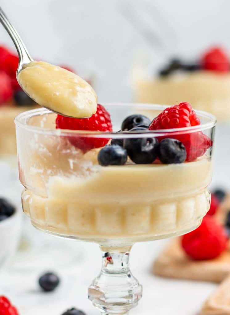 scooping out a spoonful of pudding in a glass container with berries on top and around it