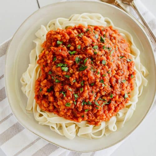 overhead of pasta with sauce on plate garnished with parsley and with two forks to the right