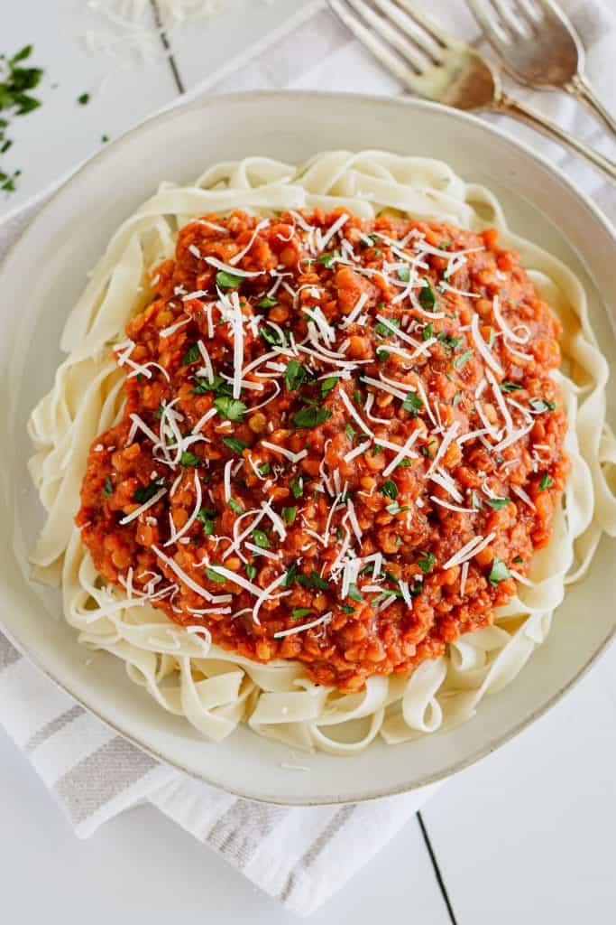 overhead of tagliatelle with sauce garnished with parsley and Parmesan cheese and two forks off to the right