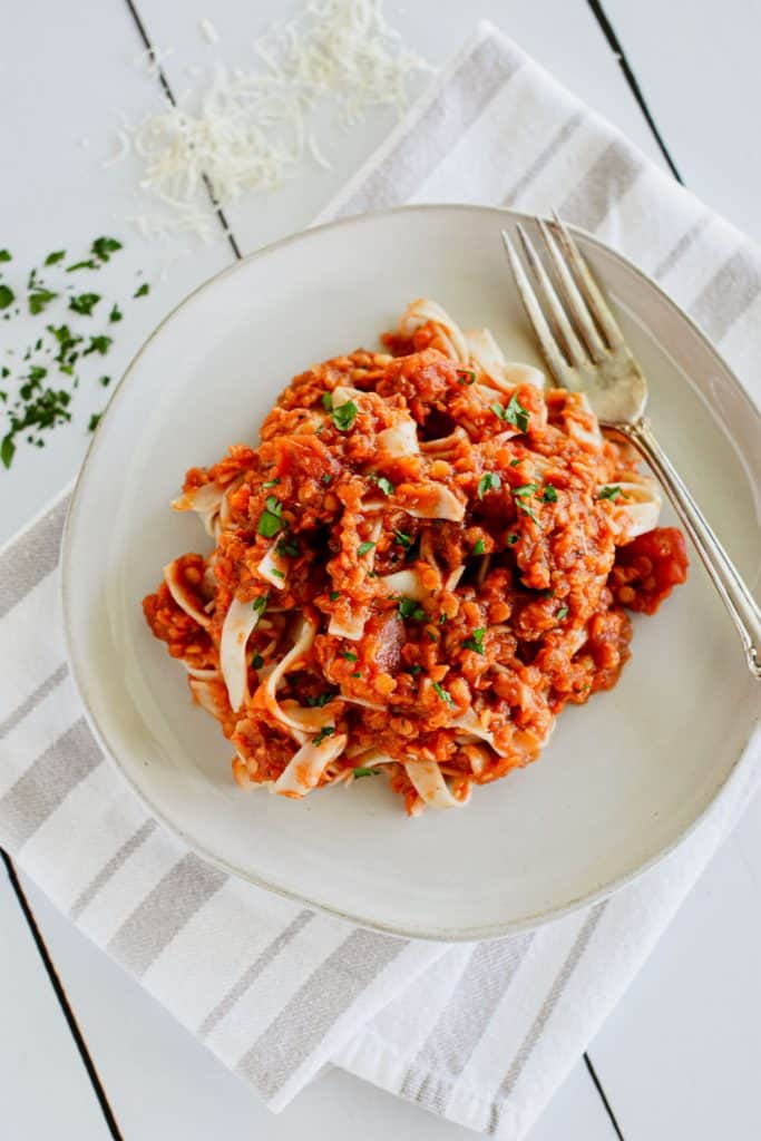 overhead of pasta with sauce on a plate with a fork garnished with parsley and some parsley and Parmesan off to the side