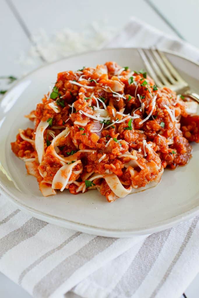 tagliatelle mixed with sauce on a plate with a fork and topped with parsley and Parmesan