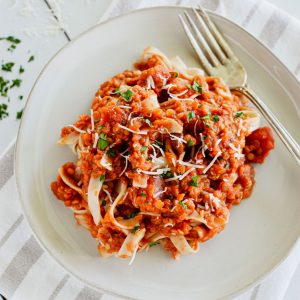 overhead of serving of pasta mixed with sauce topped with cheese and parsley