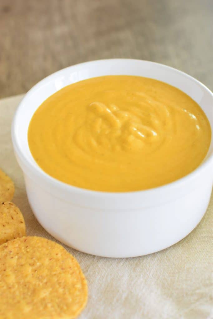 cheese sauce in white serving bowl with tortilla chips around it