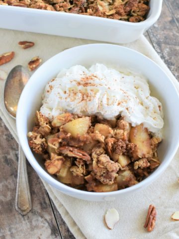 overhead of pear crisp with non-dairy whipped topping and some nuts around it and a spoon next to it