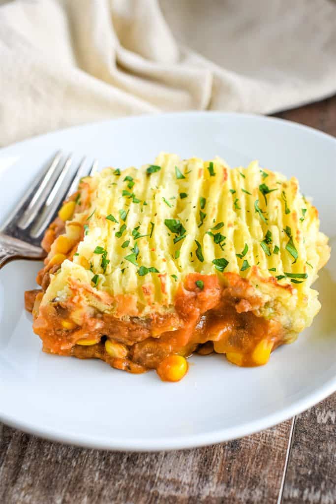 front view of piece of shepherd's pie on white plate with fork and kitchen napkin in background