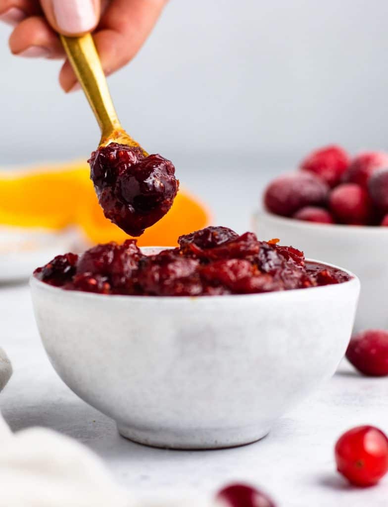 scooping some cranberry sauce out of white serving bowl with a gold spoon