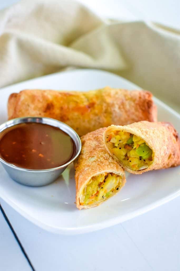 open egg roll on a plate with a closed one behind it and dipping sauce.