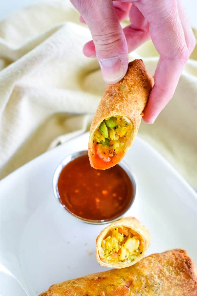 holding up an egg roll after dipping in sweet chili sauce.