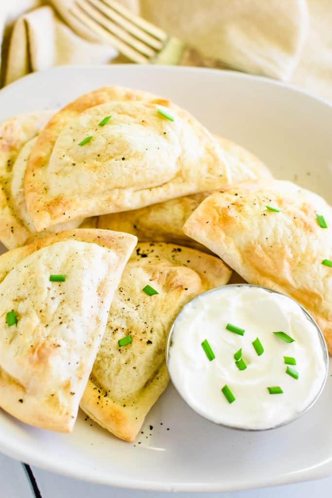 close-up overhead of pierogies one white plate with side of sour cream