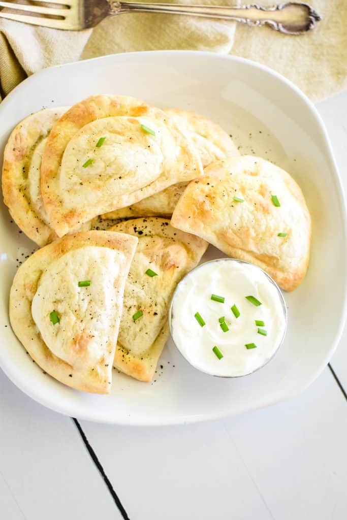 farther away overhead of pierogies on white plate with side of sour cream