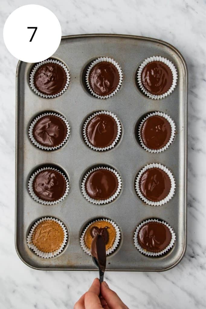 adding the second layer of chocolate on top of the peanut butter layer in the cupcake liners