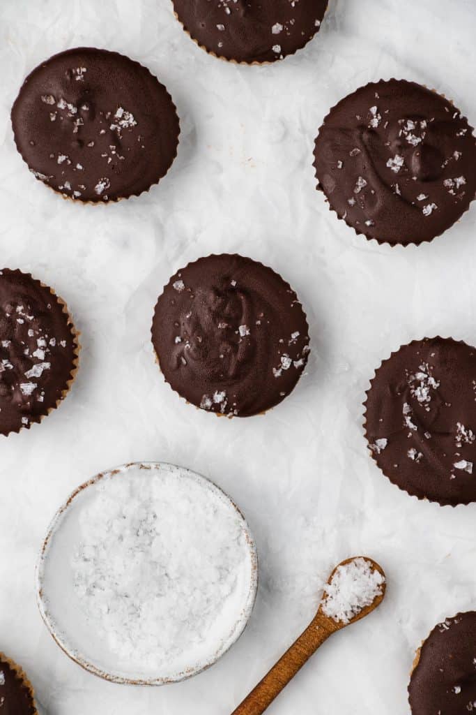 overhead of peanut butter cups on a marble surface with a bowl of sea salt and spoon with sea salt