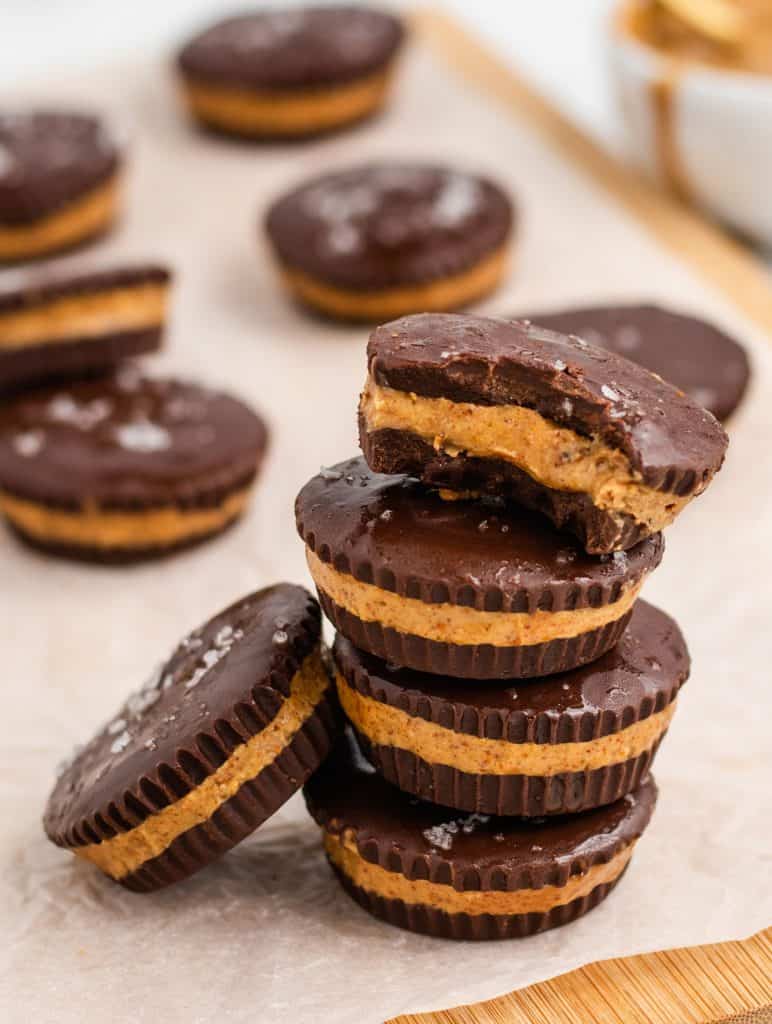 stack of peanut butter cups with bite taken out of the one on top and one leaning up against the stack and some blurred out in the background