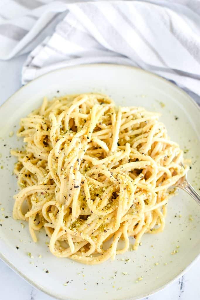 close-up overhead of pasta on white plate garnished with pepper and pumpkin seed Parmesan with fork twirling some pasta on the right