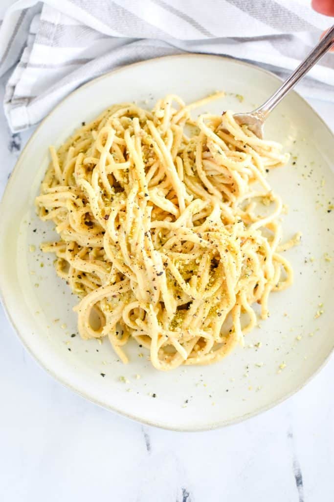 overhead shot holding a fork that is twirling some of the pasta on a white plate