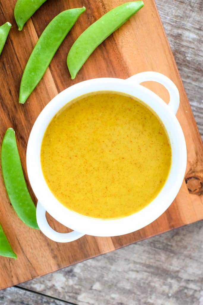 dipping sauce in white serving bowl on wooden board with snap peas around it