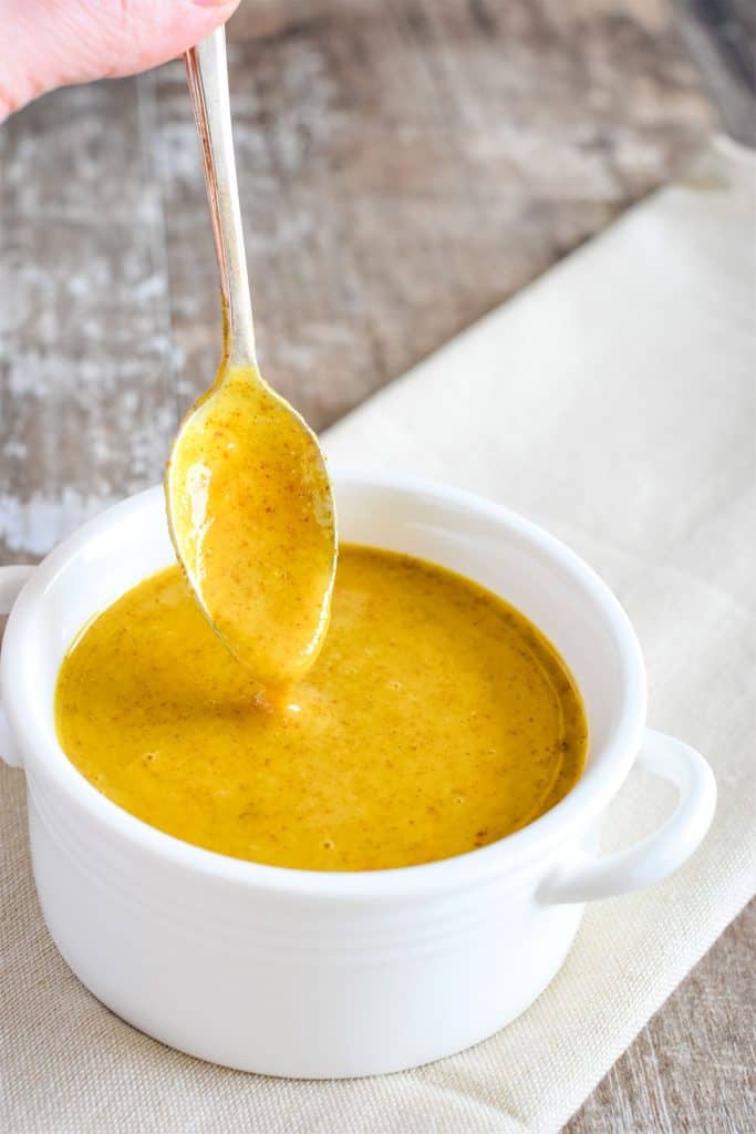 dressing dripping off spoon being held over bowl of the rest of it