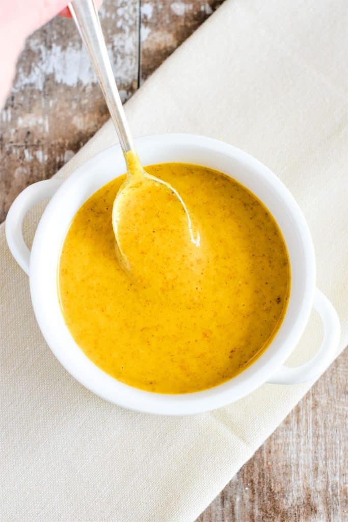 holding spoon scooping up some dressing from white bowl