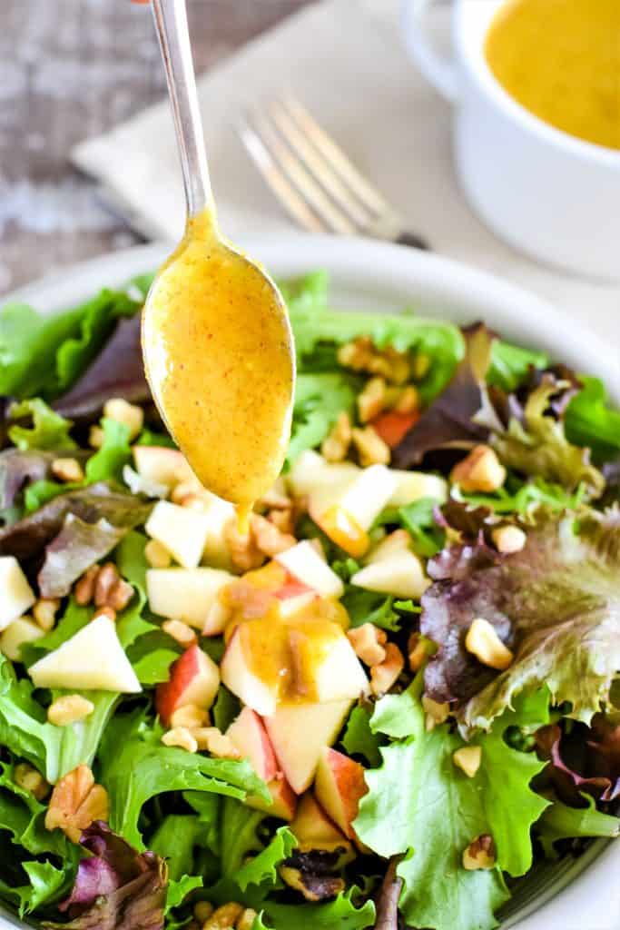 dressing dripping off spoon being held over a salad in a white bowl