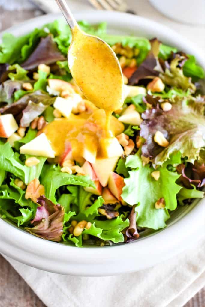 drizzling dressing with a spoon onto a salad in a white bowl