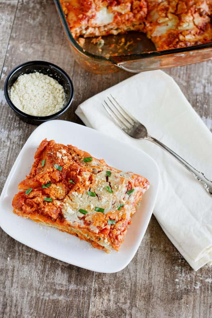 overhead of slice of lasagna on white plate garnished with basil and vegan Parmesan