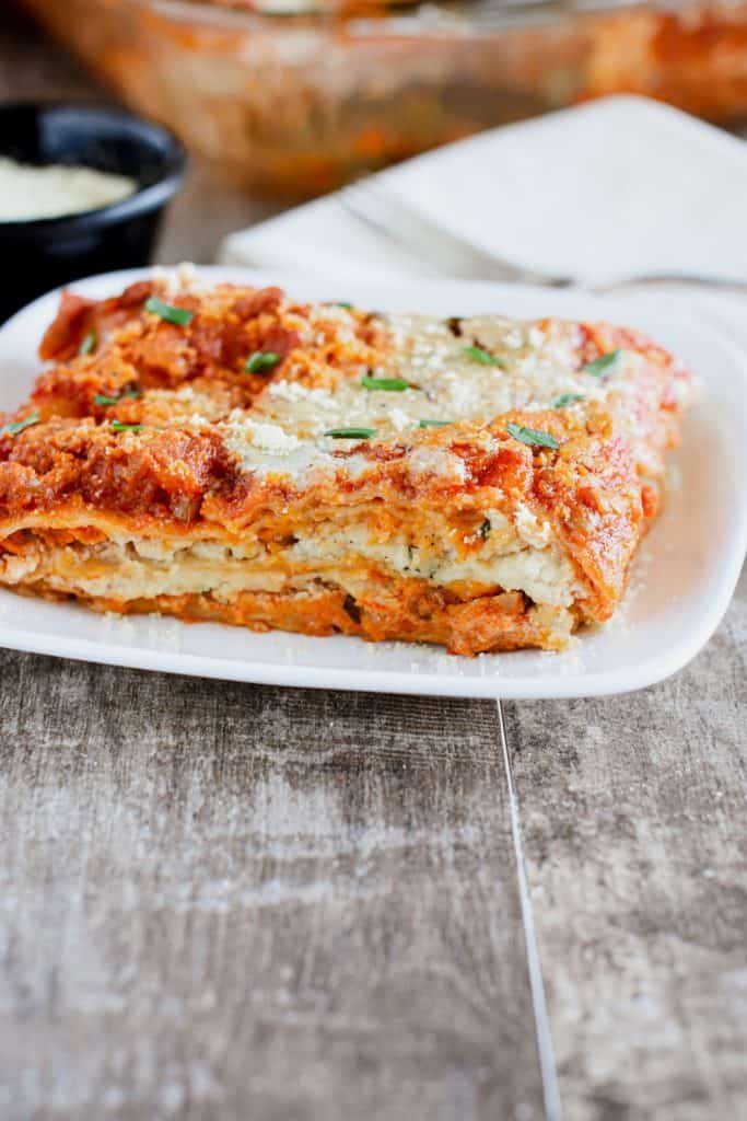 front view of slice of lasagna on a white plate garnished with basil and vegan Parmesan cheese