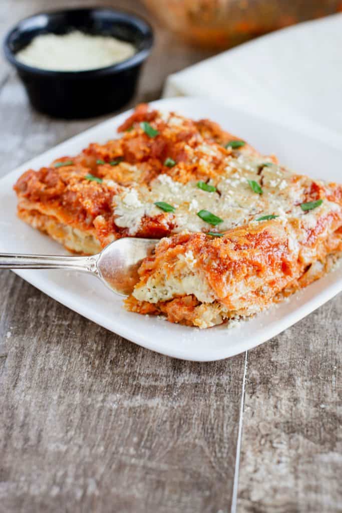 piece of vegan lentil lasagna on a plate with a fork cutting into it