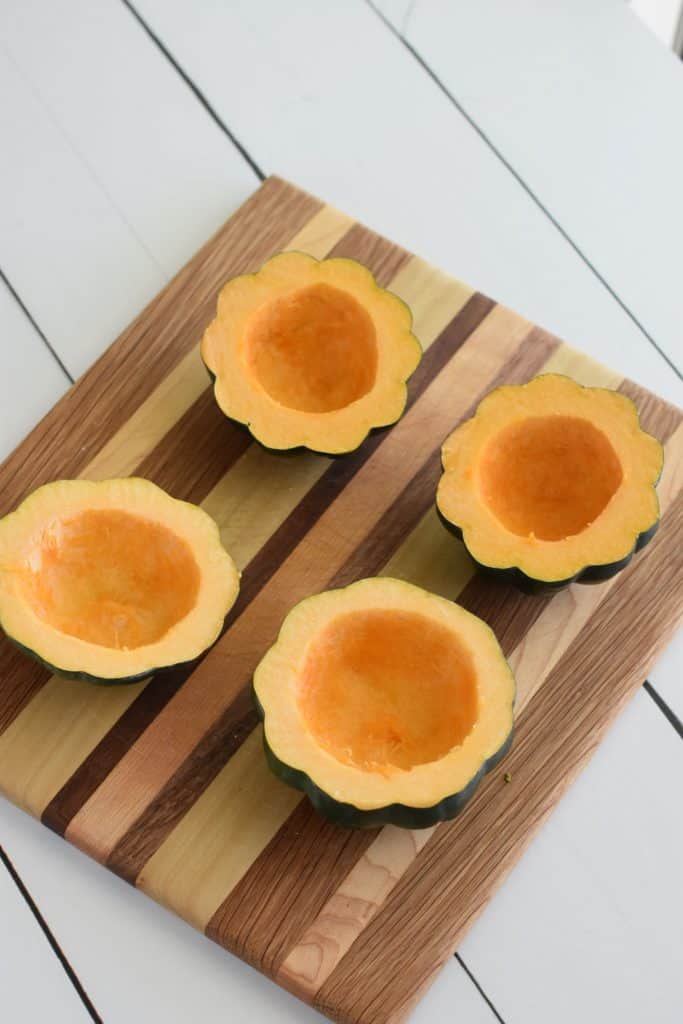 4 acorn squash halves after removing seeds on wooden board