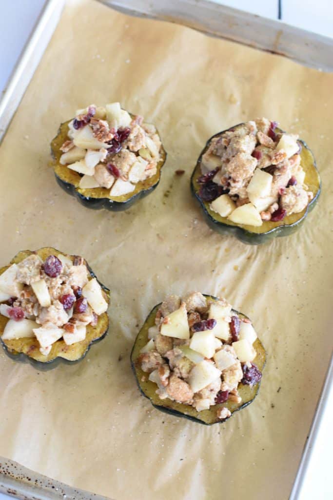 4 cooked acorn squash halves filled with stuffing mixture on parchment-lined baking sheet